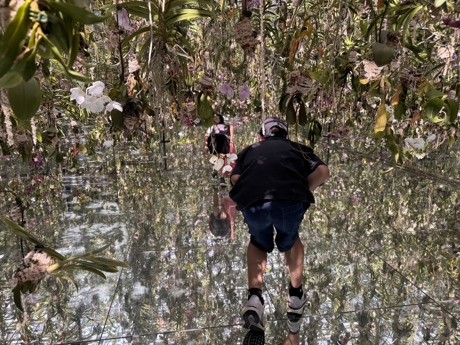 Visitors wearing shoes on the mirrored floor of the Floating Flower Garden at teamLab Planets