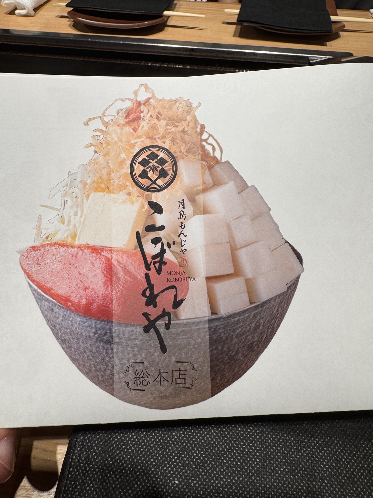 A paper menu showing monjayaki dishes served heaped high in black bowls