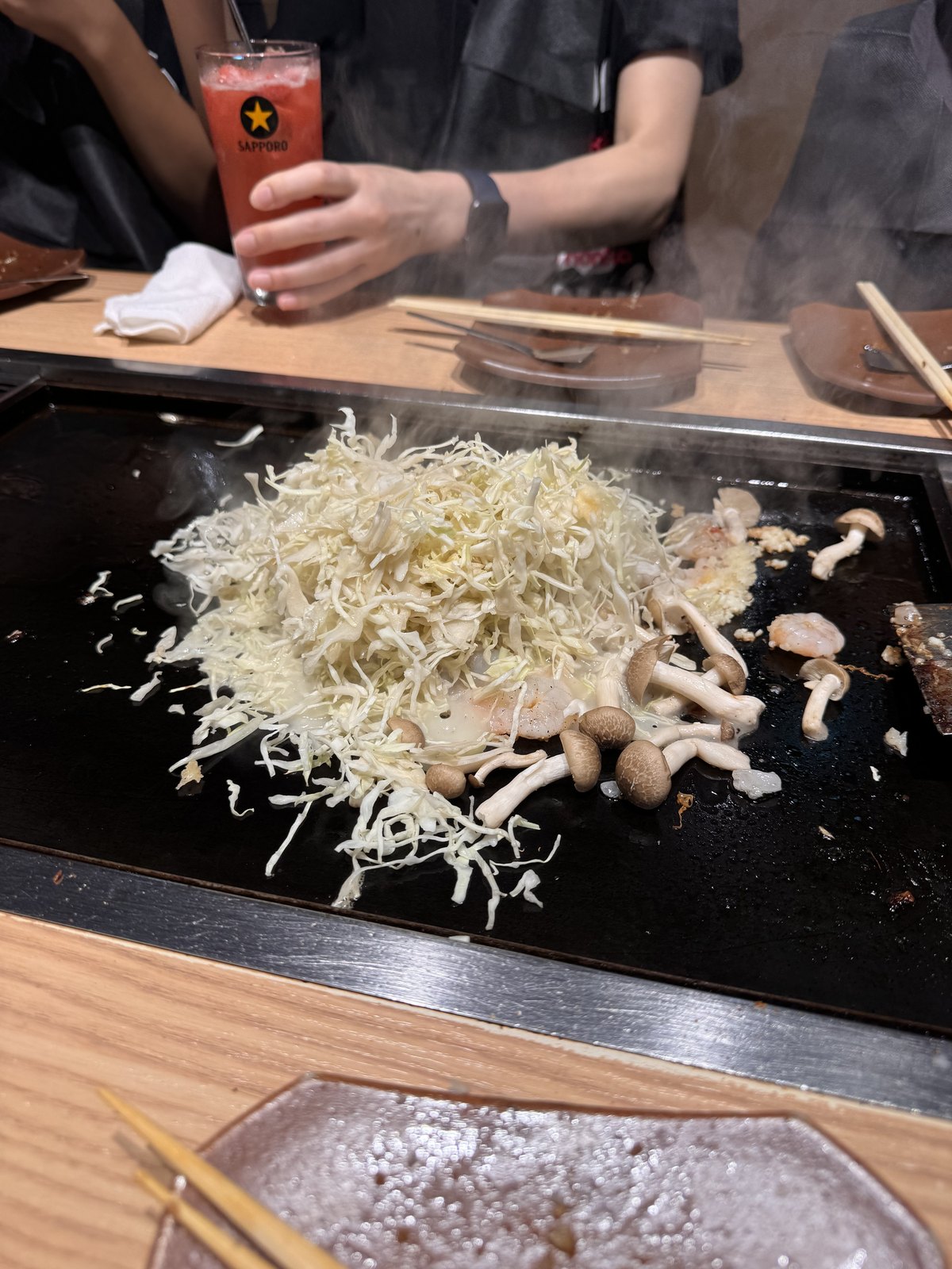 Staff spreading the ingredients for monjayaki across a hot griddle