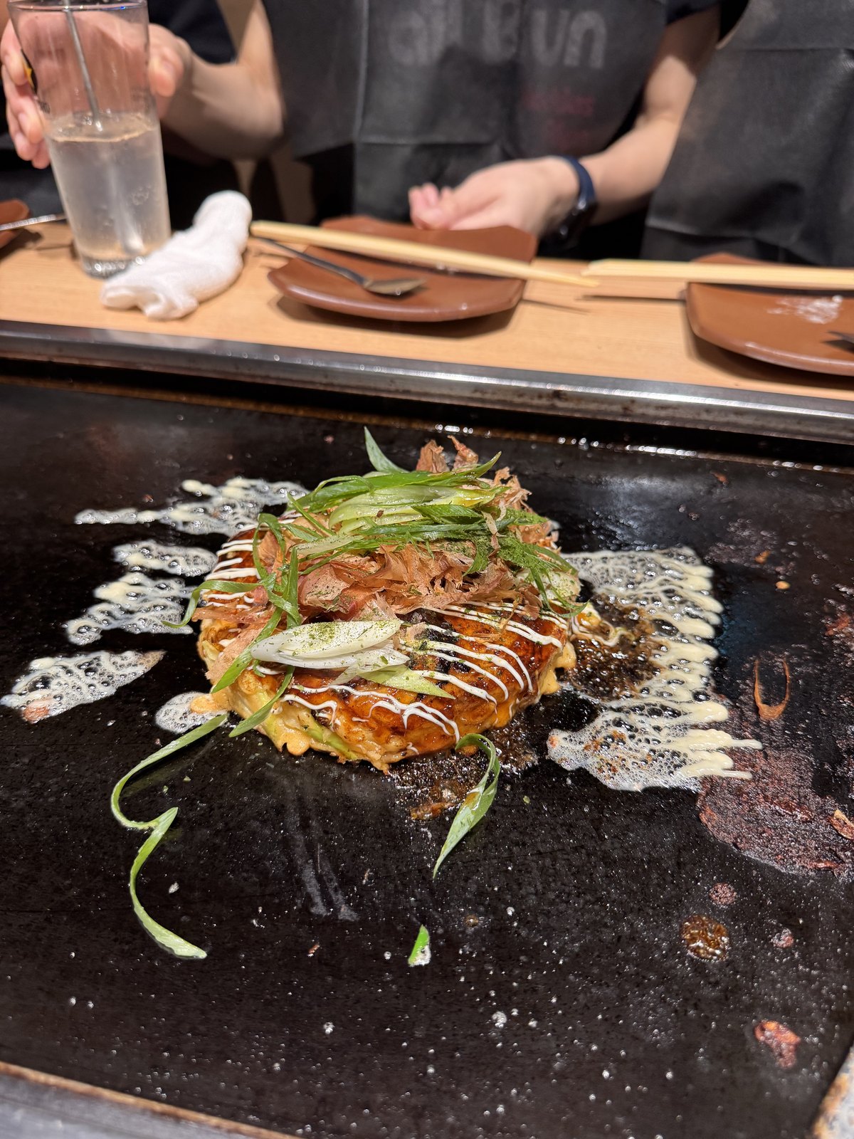 Okonomiyaki with sauce and spring onion cooking on a table hotplate